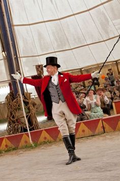 a man in a red coat and top hat is performing a trick on a pole