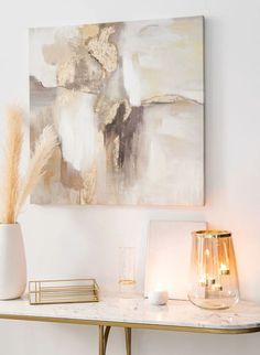 a table with some candles and a painting on the wall behind it in a white room