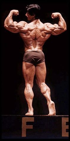 a bodybuilding man standing on top of a wooden platform with his hands behind his back