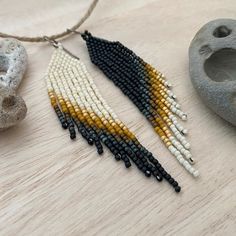 the beaded earrings are next to a rock and some beads on a wooden table