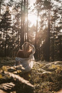 a woman standing in the middle of a forest drinking from a water bottle while looking up into the sky