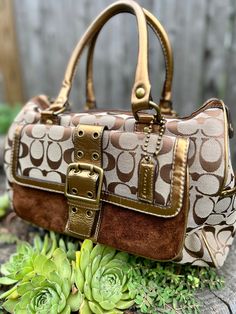 "A signature \"C\" top-handle satchel by Coach, released in 2004 Brown and tan fabric body, 4 feet on bottom, exterior pocket with milk chocolate colored suede facing and magnetic closure with decorative buckle, suede trim around top zipper, bronze leather details (handles, pulls, hang tag, trimmings), exterior pocket on each end with toggle closure, dark brown interior with large zippered pocket on one side and a trio of small pockets on the other, embossed leather certificate of authenticity s Dark Brown Interior, Clothes Game, Western Goth, Handbag Ideas, Small Hand Bags, Vintage Coach Bag, Hand Bags For Women, Quilt Coat, Tan Fabric