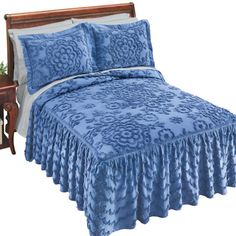 a bed with blue bedspread and pillows on it next to a night stand