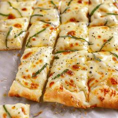 sliced pizza with cheese and herbs on it sitting on a baking sheet, ready to be eaten