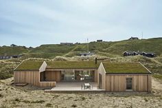 a house with green roof and grass on the top of it's roof is surrounded by sand dunes