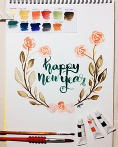 a happy new year card with watercolors and paintbrushes next to it