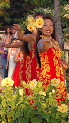 two women in red and yellow dresses are dancing with flowers on their hands while others look on