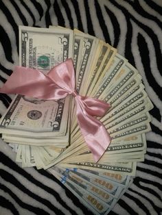 a bunch of money sitting on top of a zebra print table cloth with a pink ribbon