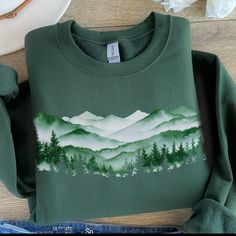 This misty mountain forest design is printed directly on a classic Gildan unisex sweatshirt with drop sleeves. When you think of a sweatshirt, this is one that should come to mind. If you prefer an oversized look, go up 1-2 sizes.  As all of our shirts are made to order, there are no refunds - make sure you are ordering the correct size. If there is any problem whatsoever with the printing or the garment itself, please contact me for assistance.  * 50% cotton, 50% polyester * Pre-shrunk * Classi Green Crew Neck Top For Adventure, Green Cotton Outdoor Sweatshirt, Green Long Sleeve Sweatshirt For Outdoor Activities, Green Cotton Sweatshirt For Outdoor, Winter Hiking Crew Neck Top, Outdoor Long Sleeve Cotton Tops, Green Crew Neck Sweatshirt For Outdoor, Long Sleeve Graphic Print Sweatshirt For Adventure, Cotton Graphic Print Sweatshirt For Adventure