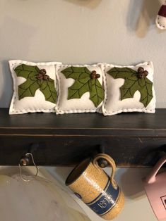 three decorative pillows are sitting on a shelf next to a coffee mug and other items