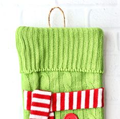 a green knitted christmas stocking hanging on a brick wall with a red button