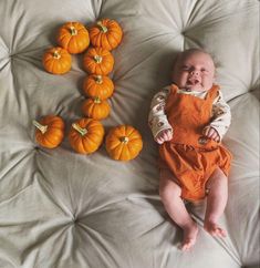 a baby laying on top of a bed next to small pumpkins in the shape of letters