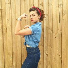 a woman posing in front of a wooden fence with her arm up and the words rose the riveter written on it