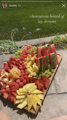 a wooden platter filled with cut up fruit on top of a stone floor next to grass