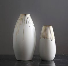 two white vases sitting on top of a black countertop next to each other