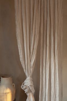 a white vase sitting on top of a table next to a curtain