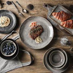 a table topped with plates and bowls filled with food next to utensils on top of a wooden table