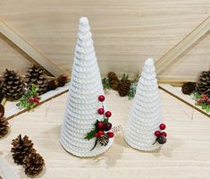 two white plastic christmas trees with red berries and pine cones on the top, surrounded by pine cones