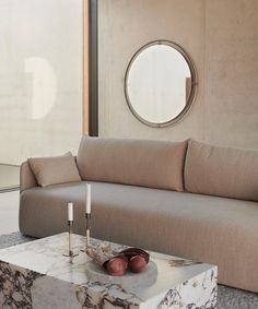 a marble coffee table with candles on it in front of a couch and round mirror