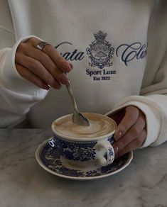 a woman is holding a spoon in a coffee cup with saucer and saucer