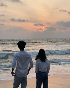 a man and woman standing on the beach watching the sun go down over the ocean