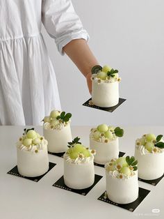 a person placing grapes on top of a white cake in the middle of eight small cakes