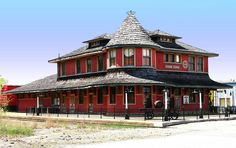 a red building with a black fence around it's corner and a clock tower on top