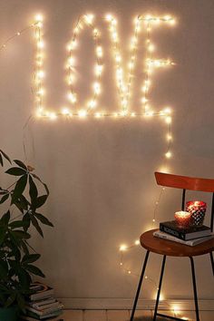 the word love spelled out in lights on a wall next to a chair and potted plant