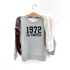 Channel your inner Miss Trunchbull with this 1972 Olympics sweatshirt. Not just for Halloween, this classic sweatshirt is perfect for any time of the year and doubles as an epic costume. Don't miss out on the funniest and most adorable wardrobe addition!! Retro Crew Sweatshirt For Fall, Retro Winter Sweatshirt For Loungewear, Retro Crew Neck Sweatshirt For Loungewear, Retro Sweatshirt For Game Day In Winter, Retro Long Sleeve Pre-shrunk Sweatshirt, Retro Winter Game Day Sweatshirt, Retro Game Day Sweatshirt For Winter, Retro Crew Neck Hoodie For Fall, Retro College Sweatshirt For Fall