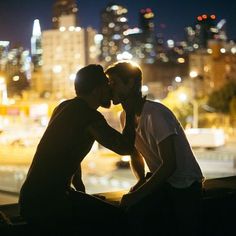 two men are kissing each other in front of a cityscape at night time