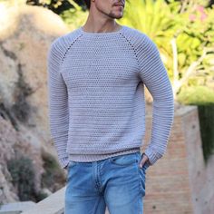 a man standing in front of a stone wall wearing a sweater and jeans with his hands on his hips