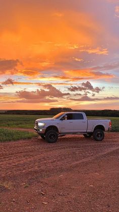 a white truck parked on the side of a dirt road near a field at sunset