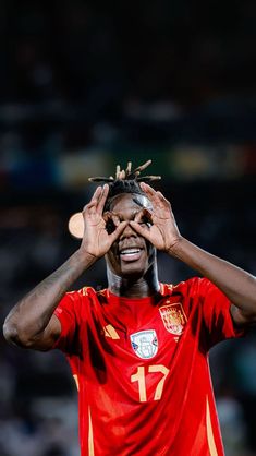 a soccer player holding his hands up to his face while wearing a red shirt and gold bracelets