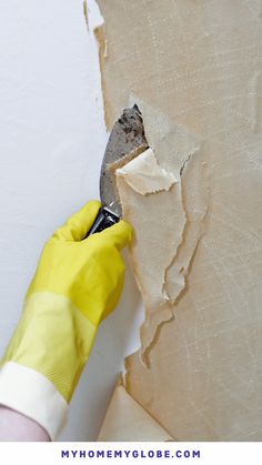 a person in yellow gloves is using a knife to paint a wall with white paint