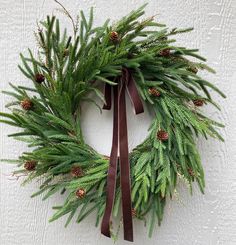 a wreath with pine cones and brown ribbon hanging on a white painted wall in the winter