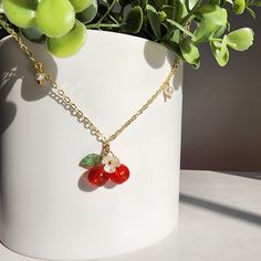 a white vase filled with green plants and two red cherries hanging from it's sides