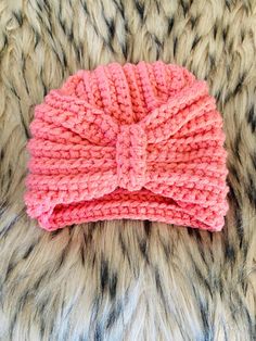 a pink knitted headband laying on top of a furry surface