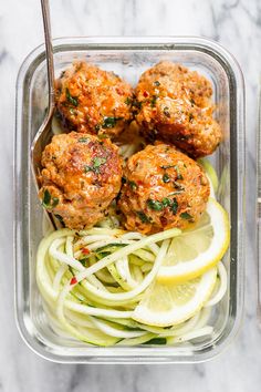 meatballs and zucchini noodles in a plastic container with lemon wedges on the side