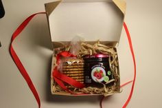 an open box with cookies, jam and crackers in it next to a red ribbon