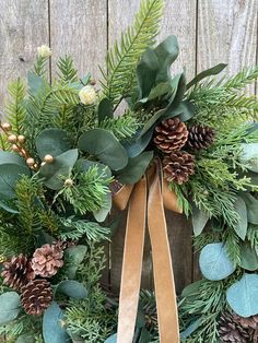 a wreath with pine cones, evergreen leaves and other greenery is hung on a wooden fence