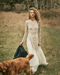 a woman in a long white dress is walking with her dog and carrying a bag