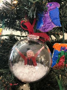 a christmas ornament hanging from a tree with snow in the bottom and an image of a child on it