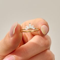 a woman's hand holding a gold ring with a flower on the side and a diamond in the middle