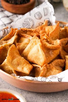 a bowl full of tortilla chips sitting on a table next to some dipping sauce