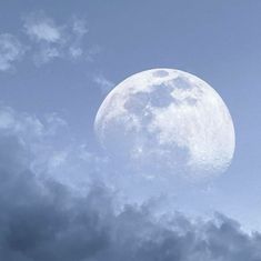 an airplane flying in the sky with a full moon behind it and dark clouds below