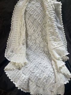 a white crocheted afghan with ruffles on the bottom and sides, sitting on top of a black sheet