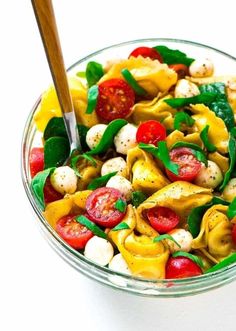 a glass bowl filled with pasta and veggies on top of a white table