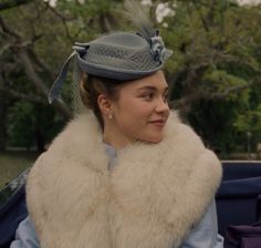 a woman in a fur stoler and hat sitting in a blue car with trees in the background