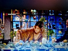 a man and woman sitting at a table in front of a television screen with christmas decorations on it