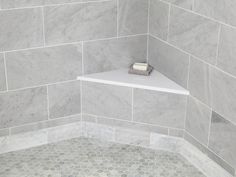 the corner of a bathroom with gray marble tile and white shelf for soap dispenser